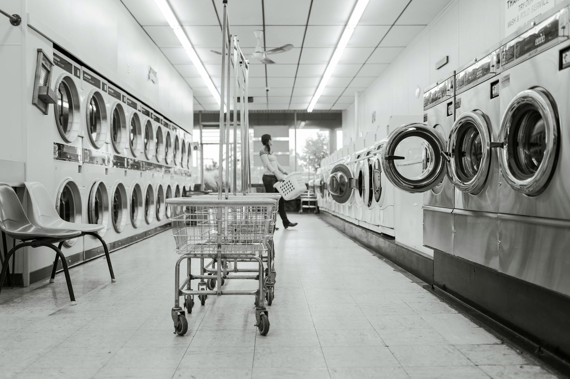 Black and white image of a laundromat with laundry machines and a person in the background.